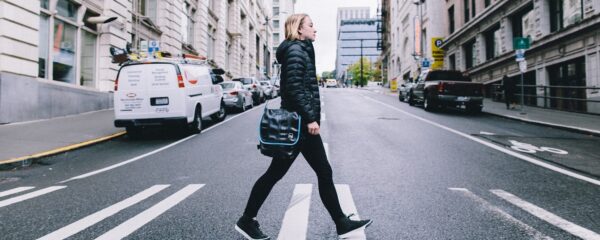 Female shown crossing city street with her crossbody shoulder bag by Alchemy Goods.