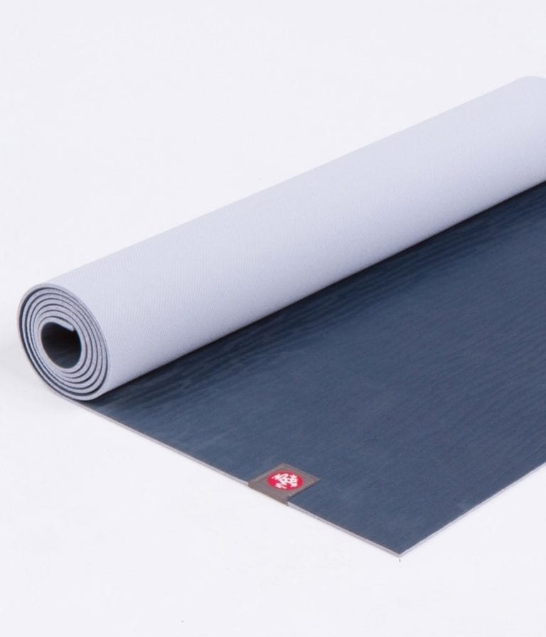 Manduka brand natural rubber 4mm yoga mat in midnight blue; partially unrolled to show both sides of mat
