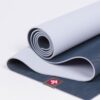Manduka brand natural rubber 4mm yoga mat in midnight blue; partially unrolled to show both sides of mat