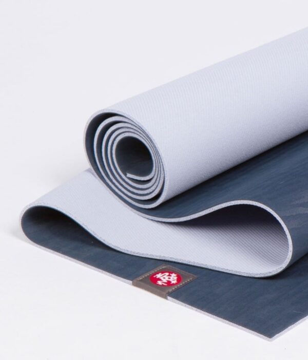 Manduka brand natural rubber 4mm yoga mat in midnight blue; partially unrolled to show both sides of mat
