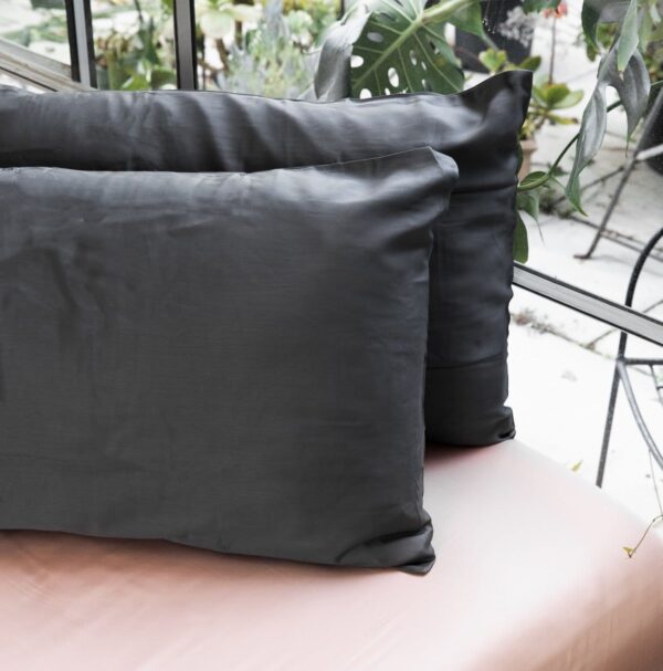 Two standard sized pillows with grey organic bamboo pillow cases resting on white ottoman up against window.  One grey organic pillow case is apart of three piece sleep travel kit made by Ettitude brand.