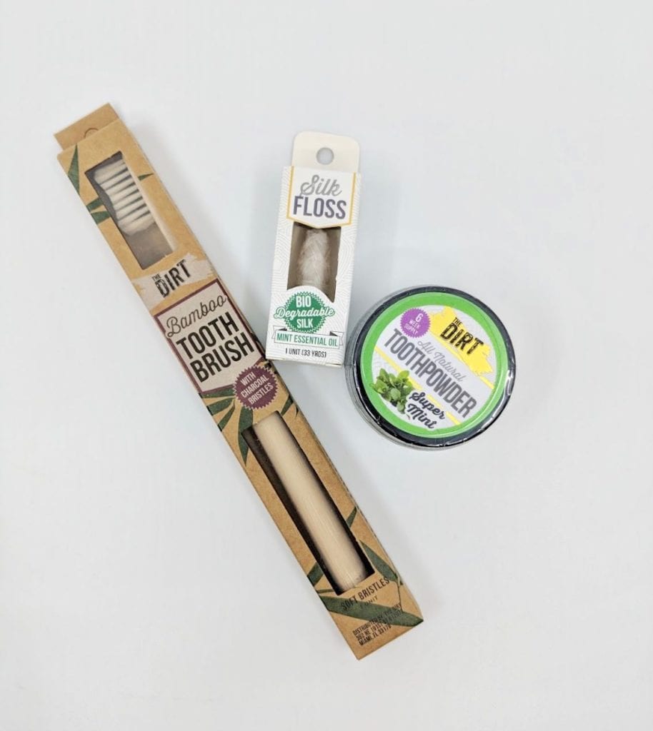 The Dirt brand eco friendly bamboo tooth brush, all natural Super Mint tooth powder, and biodegradable silk floss shown with items removed from their packaging.