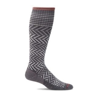 Profile product display for Sockwell brand Chevron womans moderate graduated compression sock in charcoal black with white horizontal zig zag pattern.  Sockwell brand products are made in the USA with locally sourced sustainable materials.
