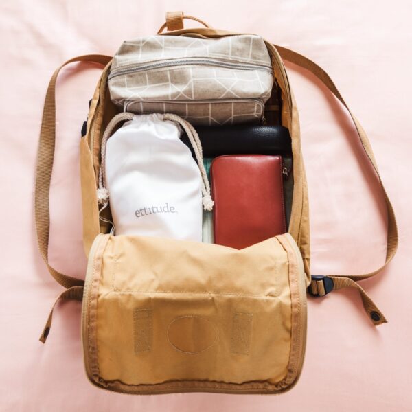 Sustainable organic bamboo white travel sheet in matching white pouch neatly packed into brown canvas overnight backpack with brown leather wallet, black leather glasses case, and a geometric design over night bag.