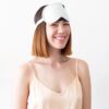 Female with short brown hair wearing white bamboo sleep mask around forehead above her eyes.  Eye mask is apart of three piece sleep travel kit made by Ettitude brand.