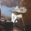 Fueling up reusable eco friendly Hydrapak brand durable shape shift 2 liter clear hydration reservoir with water on tailgate of pick up truck before heading out for a day of snowboarding.