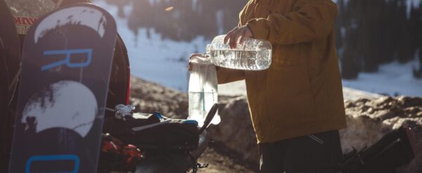 Fueling up reusable eco friendly Hydrapak brand durable shape shift 2 liter clear hydration reservoir with water on tailgate of pick up truck before heading out for a day of snowboarding.