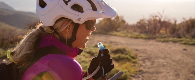 Female mountain biker fueling up on the trial with liquid from her reusable Hydrapak brand durable shape shift 2 liter clear hydration reservoir.