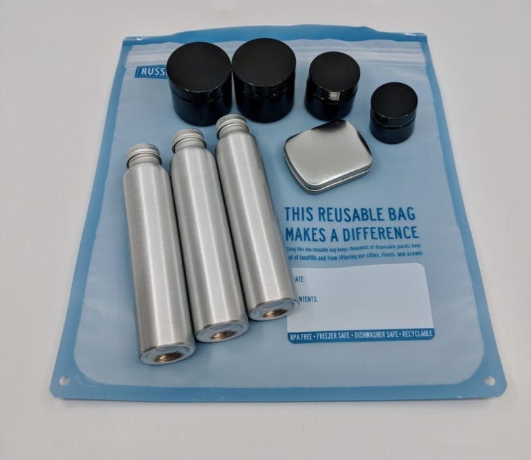 Environmentally friendly reusable TSA friendly tin and plastic containers pictured outside of blue transparent leak proof bag, part of Reusable Pack-It Travel Container Kit.