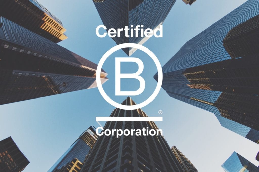 Looking up between tall buildings in city with B Corp logo