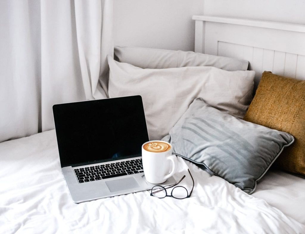 computer and coffee cup on a bed with pillows