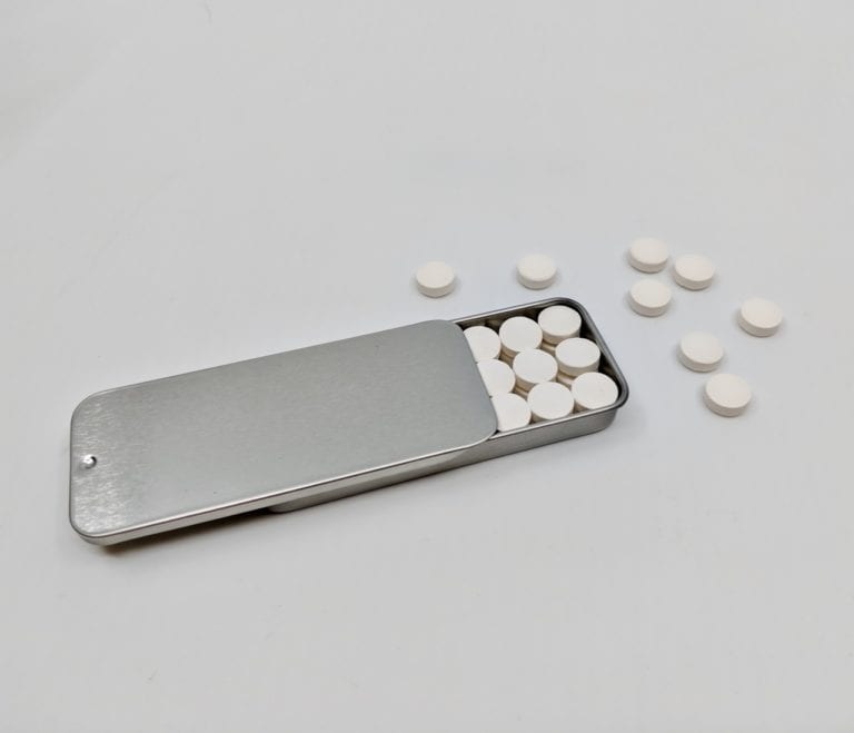 Zero-Waste Toothpaste tablets displayed below sustainable reusable tin container, made by Unpaste brand.