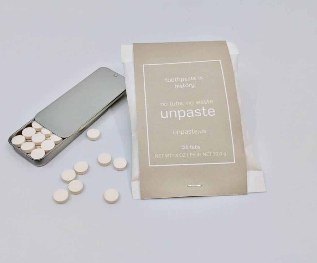 Zero-Waste Toothpaste tablets displayed below a sustainable reusable tin container next to large compostable bag of toothpaste tablets, made by Unpaste brand.