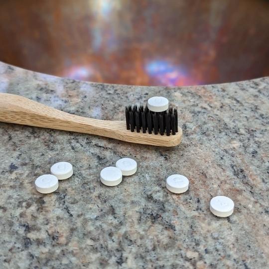 Close up of plastic-free toothpaste tablets with bamboo toothbrush