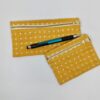 Pen laying across two earth friendly fair trade organic cotton Anchal brand mustard with white plus signs pencil cases.