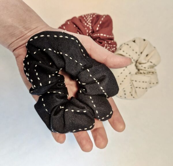 Holding an earth friendly Anchal brand charcoal scrunchie in hand, made from fair trade organic cotton with a bone and rust colored scrunchies pictured below. Sold together in 3 pack.