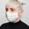 Female modeling Anchal brand organic cotton double layer face mask, bone color, that covers nose mouth and chin looped around ears to hold in place.