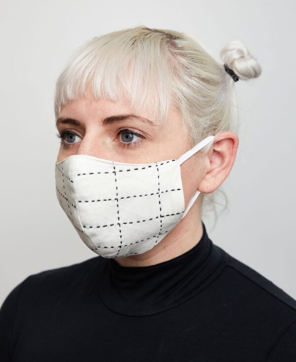 Female modeling Anchal brand organic cotton double layer face mask, bone color, that covers nose mouth and chin looped around ears to hold in place.