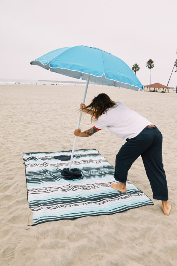 Man at beach putting umbrella into hood hole of eco-friendly Baja Aqua Poncho Towel