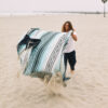 Man on beach laying out recycled Baja Aqua Poncho towel as a blanket