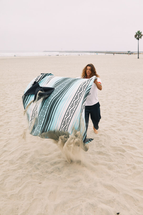 Man on beach laying out recycled Baja Aqua Poncho towel as a blanket