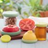 A set of five green reusable food savers, by Food Huggers, shown keeping a tomato fresh and a jar sealed.