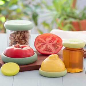 A set of five green reusable food savers, by Food Huggers, shown keeping a tomato fresh and a jar sealed.