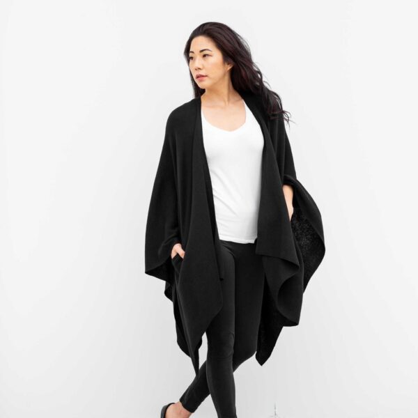 Woman with hands in pockets of black organic cotton sustainable travel blanket wrap