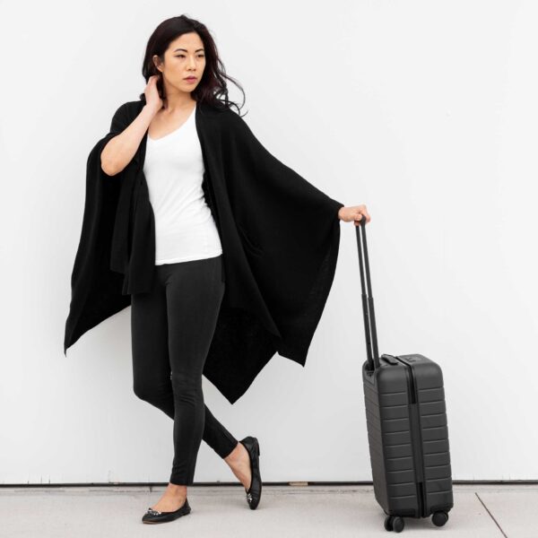 Female traveling in sustainable organic cotton black travel wrap with suitcase