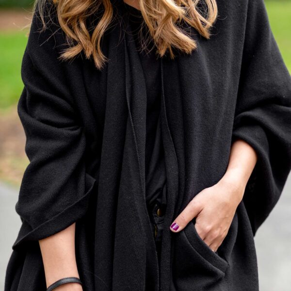 Close up on hands in the pocket of Zestt Organic's black, organic cotton blanket travel shawl wrap