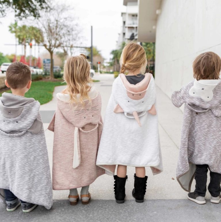 Four children modeling their organic cotton travel blankets with adorable monkey, bear, unicorn, and bunny hoods.