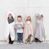 Four children modeling their organic cotton travel blankets with adorable monkey, bear, unicorn, and bunny hoods.