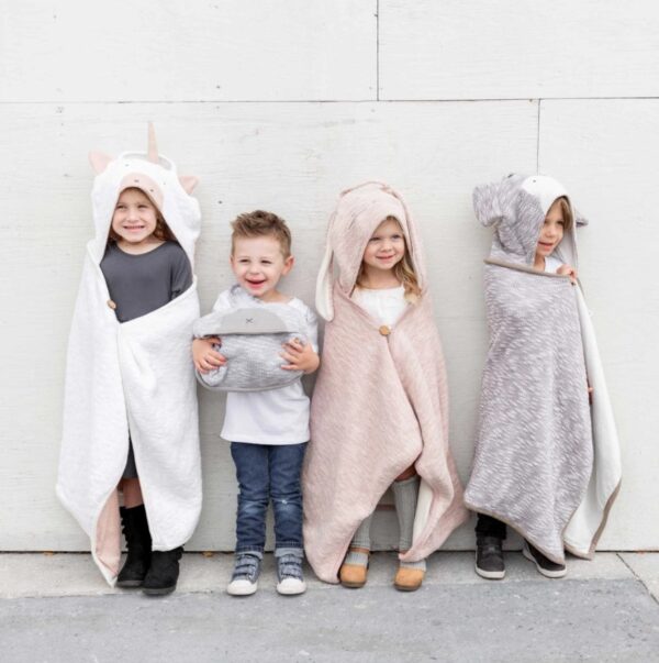 Four children modeling their organic cotton travel blankets with adorable monkey, bear, unicorn, and bunny hoods.