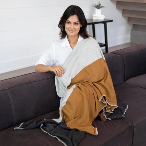 Woman standing against a white backdrop wearing her Organic Cotton Travel blanket in bronze colorblock, by Zestt Organics