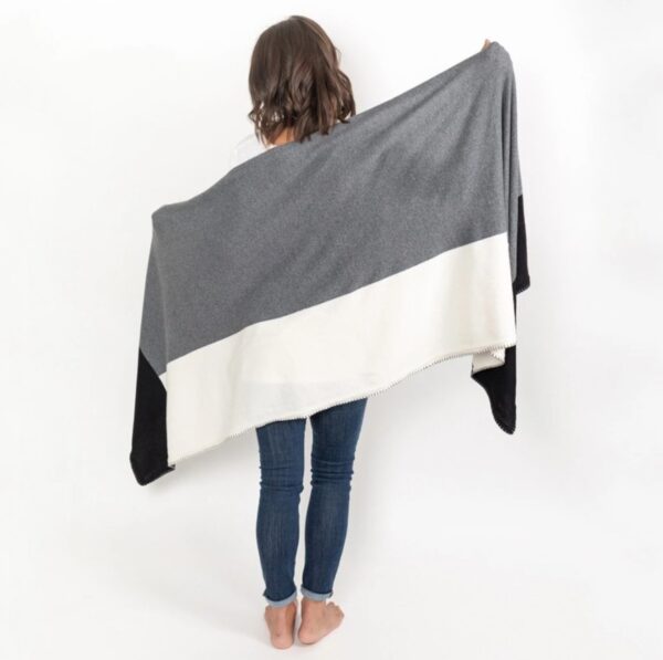 Woman standing against a white backdrop wearing her Organic Cotton Travel Shawl in gray colorblock. Certified organic cotton means fair wages and better labor standards for workers.