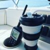 A black reusable Pokito cup is on a boat next to a marine radio; it is the perfect companion while traveling by air, land, or sea!