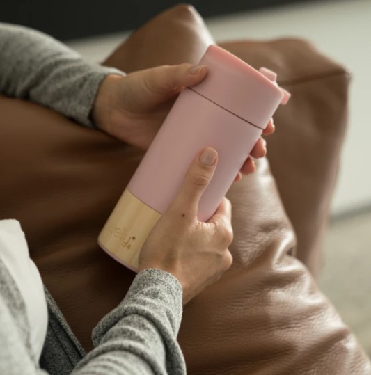 The Welly 12 oz original mug is made partially of bamboo, an easily renewable resource. Model is holding the bamboo and rose colored mug while sitting on the couch.