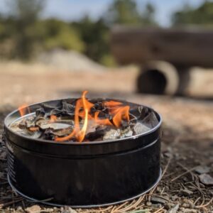 The all-natural portable campfire by Fire Lake Soapery is made of recycled paper and soy wax; shown lit at a campsite.