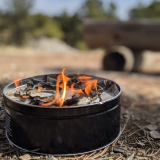 The all-natural portable campfire by Fire Lake Soapery is made of recycled paper and soy wax; shown lit at a campsite.