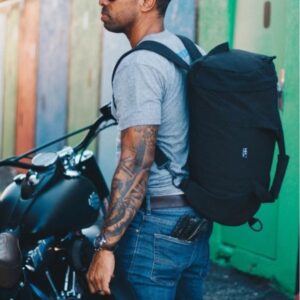 Model shown carrying the Hamilton Perkins duffle bag as a backpack, made from recycled plastic and billboard fabric.