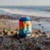 The beer blanket koozie in baja fade shown on a rock at the beach. This koozie is made from recycled materials and is earth friendly.