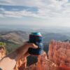 The beer blanket koozie by Rumpl is a great travel companion; shown here being held by a model while on a hike.