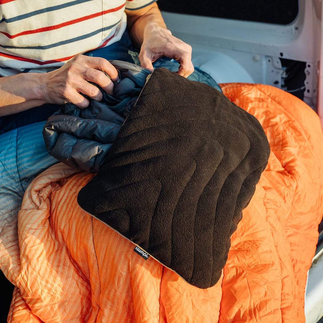RUMPL-PILLOW-BLACK-2 Photo of a model stuffing their stuffable pillowcase by Rumpl with jacket.
