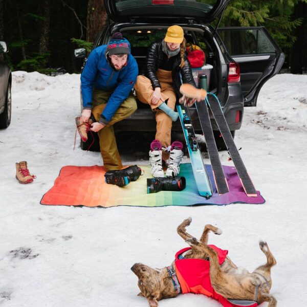 The stash mat by Rumpl, shown here being used by models to take off their ski gear while at their car, keeping their ski gear dry and clean.
