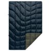 The Nanoloft Puffy Blanket by Rumpl is shown here in the Outdoor Vibes design, which features a green-gray back and a navy front with small camping icons like lantern, tent, axe, and campfire.