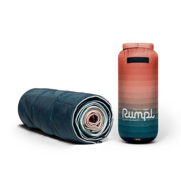The eco-friendly Nanoloft puffy blanket in patina pixel fade has a navy backing and a white binding. Its stuff sack has about 15 faded colors from pink to blue on the exterior.
