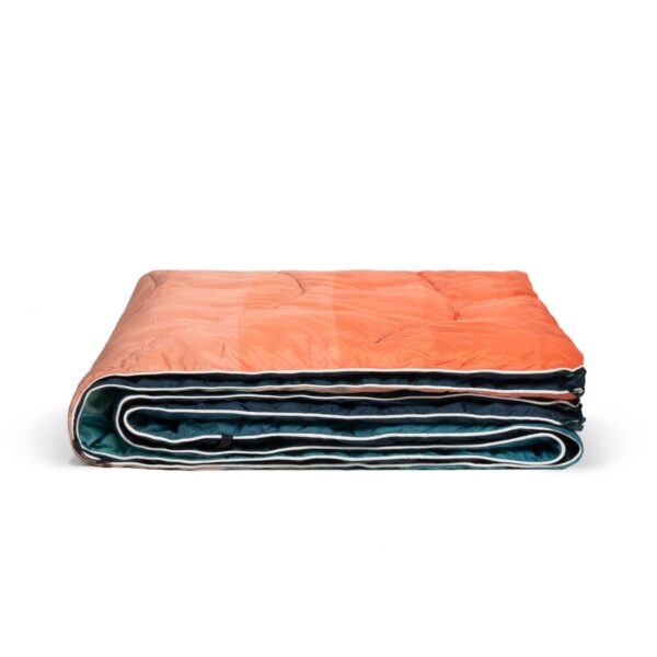 The earth friendly Nanoloft Puffy Blanket by Rumpl is shown folded, with a front that features a pixel fade pattern from pink to blue, a navy backing, and a white binding.