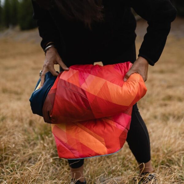 Photo of a model rolling up his eco-friendly Original Puffy Blanket by Rumpl, getting is ready to stuff into its stuff sack.
