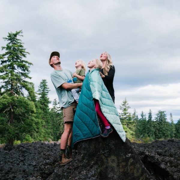 A family taking a break while on a hike. One of the kids is using the Original Puffy Blanket by Rumpl as a blanket slash cape.
