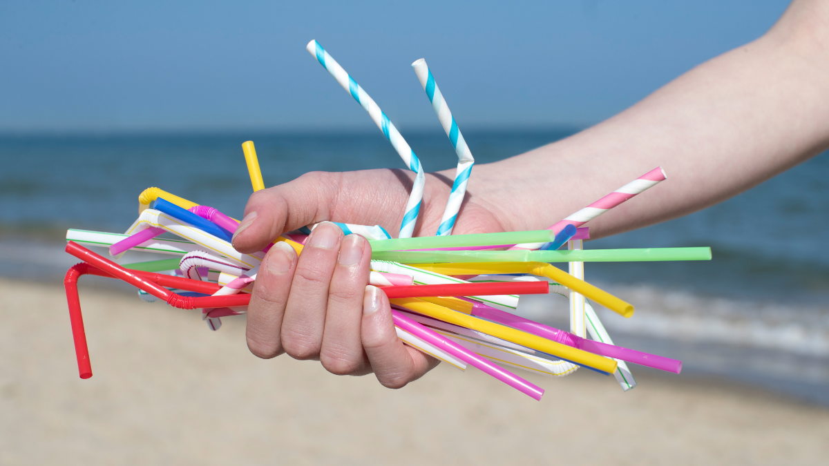 Hand holding plastic straws on beach for plastic free swaps blog